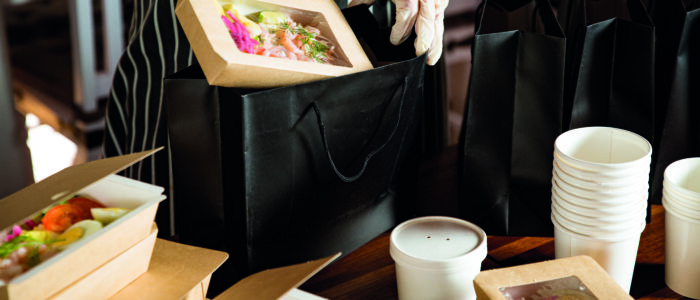 Restaurant worker wearing protective mask and gloves packing foo